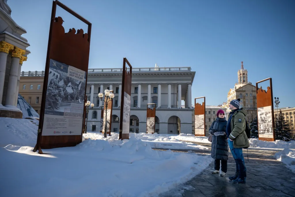 To personer står og ser på minneplakat i sentrum av Kyiv