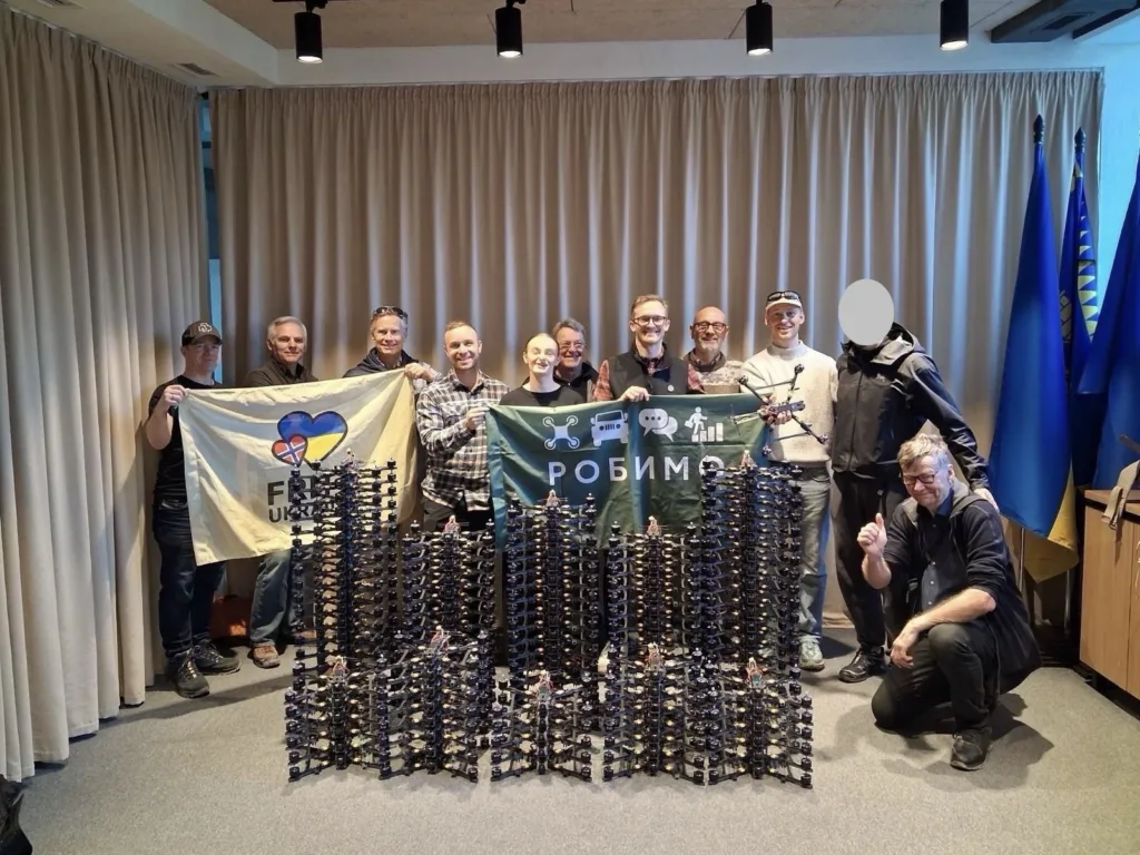 en gruppe personer med bunker av droner foran seg, ved overlevering